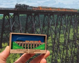 Wood carving of Kinzua Bridge held against photo of the actual bridge