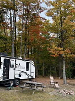 Cozy Embers wooded campground with parked trailer and picnic table